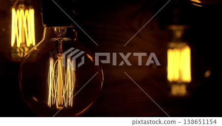 Light bulbs with glowing filaments shining in a dark setting create a warm atmosphere visible in a cozy room Light bulbs with glowing filaments shining in a dark setting create a warm atmosphere visible in a cozy room 138651154