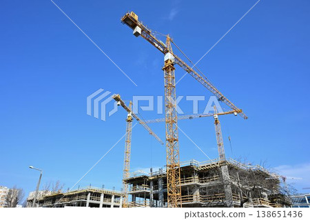 Three yellow tower cranes at a residential building construction site in a city Three yellow tower cranes at a residential building construction site in a city 138651436