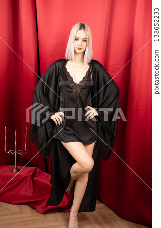 Blonde woman in black robe posing against red background Blonde woman in black robe posing against red background 138652233