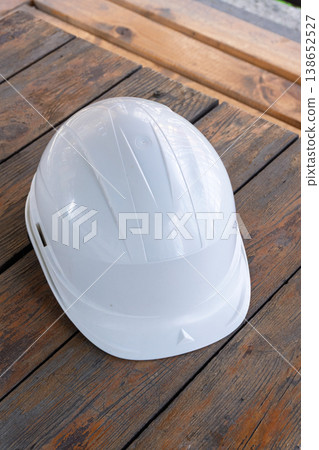 Vertical close-up of a white safety helmet on a rustic wooden table. Protective hardhat for construction and engineering work. Industrial background Vertical close-up of a white safety helmet on a rustic wooden table. Protective hardhat for construction and engineering work. Industrial background 138652527