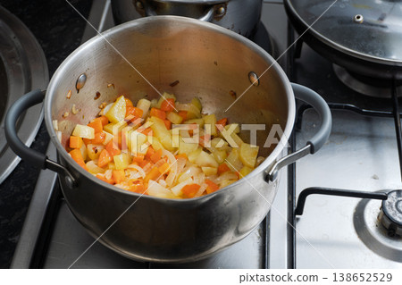 Healthy vegan meal preparation with chopped root vegetables on a gas stove Healthy vegan meal preparation with chopped root vegetables on a gas stove 138652529