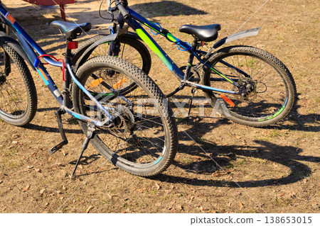 Two modern mountain bikes parked on a dirt path in a sunny park. Two modern mountain bikes parked on a dirt path in a sunny park. 138653015