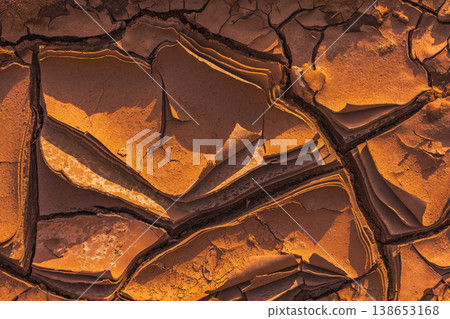 Cracked Earth. An arid landscape with cracked, dry earth patterns in a warm orange hue 138653168