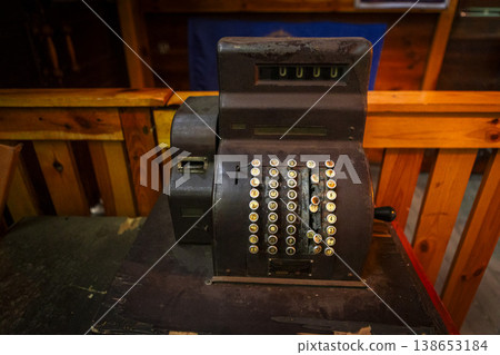 Classic black cash register elegantly displayed on a rustic wooden table in a cozy caf setting. Classic black cash register elegantly displayed on a rustic wooden table in a cozy caf setting. 138653184