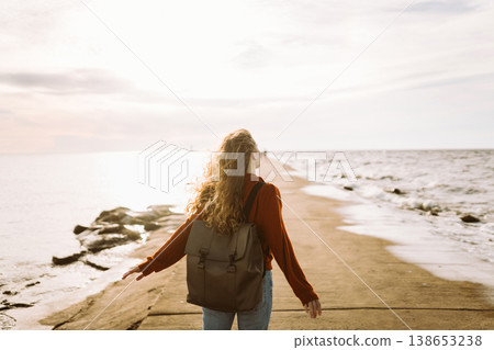 Woman enjoying breezy day near vibrant red lighthouse at sunset. Travel, weekend, lifestyle concept. Woman enjoying breezy day near vibrant red lighthouse at sunset. Travel, weekend, lifestyle concept. 138653238