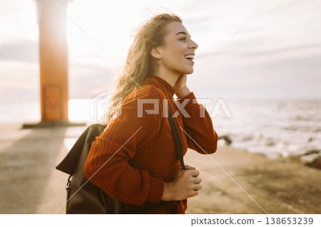 Woman enjoying breezy day near vibrant red lighthouse at sunset. Travel, weekend, lifestyle concept. Woman enjoying breezy day near vibrant red lighthouse at sunset. Travel, weekend, lifestyle concept. 138653239