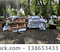Bags of construction materials are stacked and pallets are piled in a city yard or park. 138653433