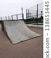 An old skate ramp in an outdoor park with a metal roof and fencing in the background. 138653445