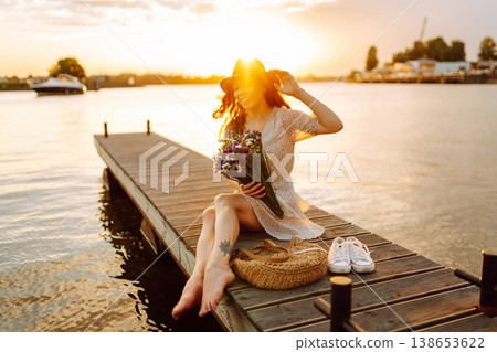 Young woman in dress sitting on wooden pier near pond. Rustic style of wedding. Travel, tourism Young woman in dress sitting on wooden pier near pond. Rustic style of wedding. Travel, tourism 138653622