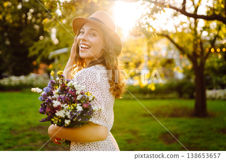 Happy woman strolled through park, carrying bouquet of freshly picked wildflowers. Fashion style. Happy woman strolled through park, carrying bouquet of freshly picked wildflowers. Fashion style. 138653657