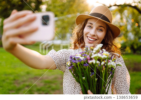 Young woman with blossoming flower bouquet taking selfie on cellphone outdoor. Blogging concept. 138653659