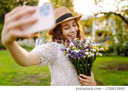 Young woman with blossoming flower bouquet taking selfie on cellphone outdoor. Blogging concept. Young woman with blossoming flower bouquet taking selfie on cellphone outdoor. Blogging concept. 138653660