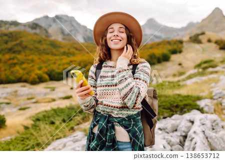 Woman is seen smiling, holding yellow phone in autumn landscape. Enjoying fresh air after hiking. Woman is seen smiling, holding yellow phone in autumn landscape. Enjoying fresh air after hiking. 138653712