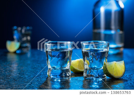 Vodka with lime slices on a black stone table. Vodka with lime slices on a black stone table. 138653763