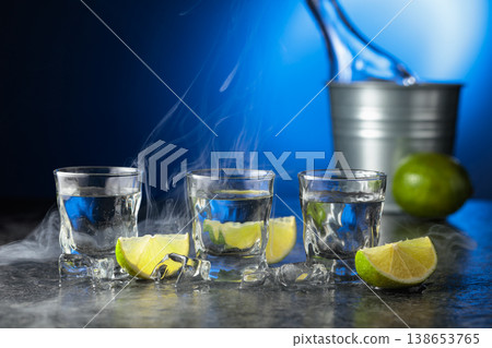 Vodka with lime slices on a black stone table. 138653765