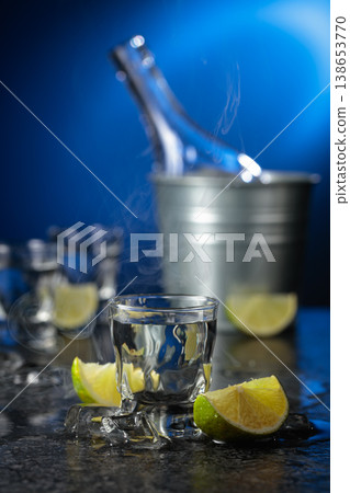 Vodka with lime slices on a black stone table. 138653770