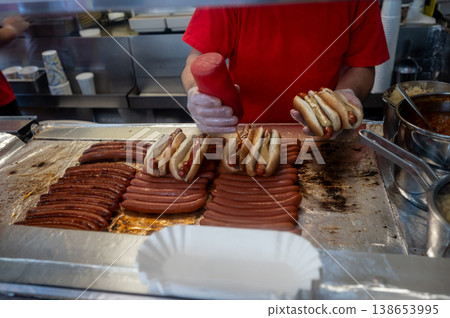 New york, usa august 14,2024. Vendor preparing multiple hot dogs on a grill, adding mustard and ketchup, showcasing american street food and fast food culture New york, usa august 14,2024. Vendor preparing multiple hot dogs on a grill, adding mustard and ketchup, showcasing american street food and fast food culture 138653995