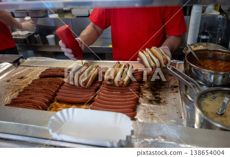 New york, usa august 14,2024. Vendor hands preparing hot dogs with mustard and ketchup, showcasing popular street fast food preparation at a typical concession stand New york, usa august 14,2024. Vendor hands preparing hot dogs with mustard and ketchup, showcasing popular street fast food preparation at a typical concession stand 138654004