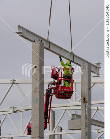 Worker guiding steel beam into place on concrete columns at industrial construction site crane lift Worker guiding steel beam into place on concrete columns at industrial construction site crane lift 138654040