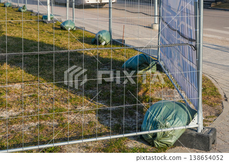 Metal temporary fence secured with sandbags along sidewalk construction site safety boundary line Metal temporary fence secured with sandbags along sidewalk construction site safety boundary line 138654052