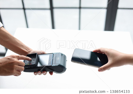 Copped hands of people using a smartphone to pay by holding close to a point-of-sale (POS) terminal. Contactless payment transaction is a fast and secure way to pay. 138654133