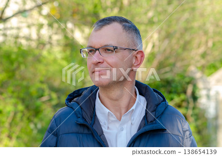 Adult man aged 51 wearing glasses poses outdoors with greenery and nature background 138654139