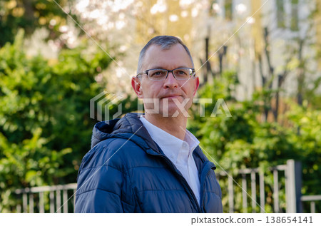 Man wearing glasses stands outdoors full length in jacket and looks at camera Man wearing glasses stands outdoors full length in jacket and looks at camera 138654141