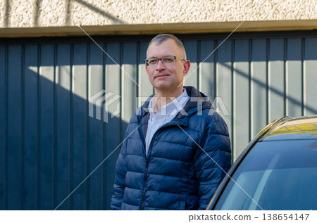 Man wearing glasses stands outdoors with metal gate background in jacket looking confident Man wearing glasses stands outdoors with metal gate background in jacket looking confident 138654147