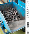 Collection of metal gears and sprockets stored in a blue industrial bin at a tractor manufacturing plant 138654204