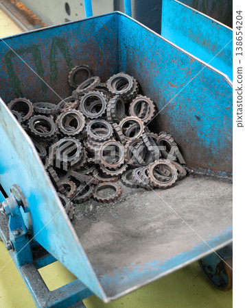 Collection of metal gears and sprockets stored in a blue industrial bin at a tractor manufacturing plant 138654204