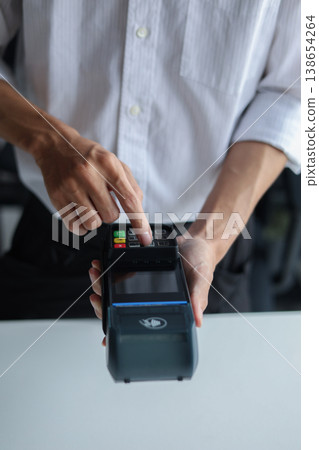 A person using a point-of-sale (POS) terminal, also known as a credit card machine to process a transaction. A person using a point-of-sale (POS) terminal, also known as a credit card machine to process a transaction. 138654264