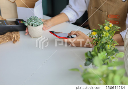 A shop owner or employee using phone checking order or to document the plant for inventory. A shop owner or employee using phone checking order or to document the plant for inventory. 138654284