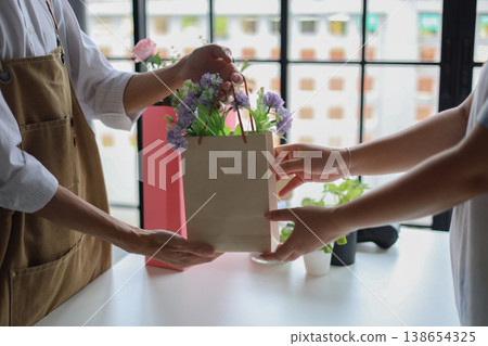 A florist or shop owner, handing a paper bag containing flowers to a customer.Flower shop, small business, retailing concept. A florist or shop owner, handing a paper bag containing flowers to a customer.Flower shop, small business, retailing concept. 138654325