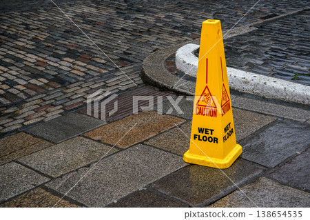 Yellow cone with caution slippery surface sign, on wet stone tiles pavement Yellow cone with caution slippery surface sign, on wet stone tiles pavement 138654535