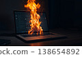 A laptop screen on a dark desk bursting into flames—a symbol of online firestorms. 138654892