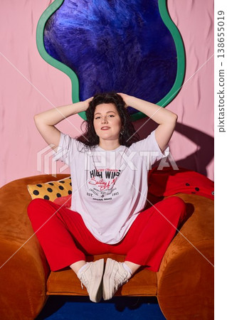 Female seated on orange couch beneath gentle spotlight with vibrant decor Female seated on orange couch beneath gentle spotlight with vibrant decor 138655019
