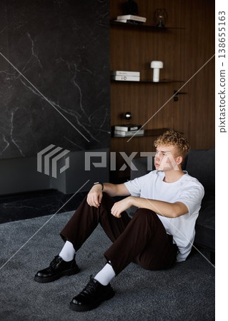 Youthful man sitting calmly in minimalist interior setting Youthful man sitting calmly in minimalist interior setting 138655163