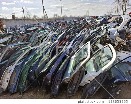 Rows of used car doors in various colors and models are organized in a large outdoor salvage yard. The doors are waiting to be sold and reused by customers. 138655365