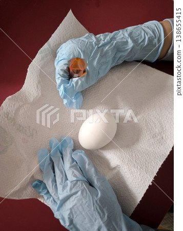 The process of dyeing a white egg with food coloring while wearing blue protective gloves The process of dyeing a white egg with food coloring while wearing blue protective gloves 138655415