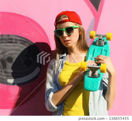 Stylish young girl with skateboard in glasses, modern teenager girl posing against the graffiti wall Stylish young girl with skateboard in glasses, modern teenager girl posing against the graffiti wall 138655455