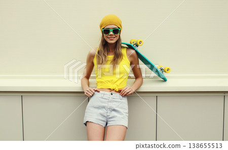 Stylish young woman with skateboard smiles, happy modern teenage girl posing on white wall Stylish young woman with skateboard smiles, happy modern teenage girl posing on white wall 138655513