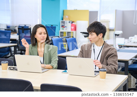 Businesswomen contemplating while working on their PCs side-by-side in a free-address office. 138655547