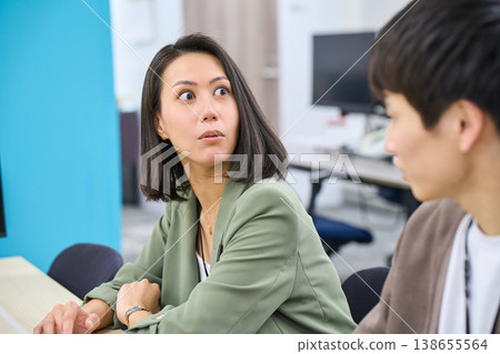A female senior colleague gives advice to a male employee who is working on his computer in the office. A female senior colleague gives advice to a male employee who is working on his computer in the office. 138655564