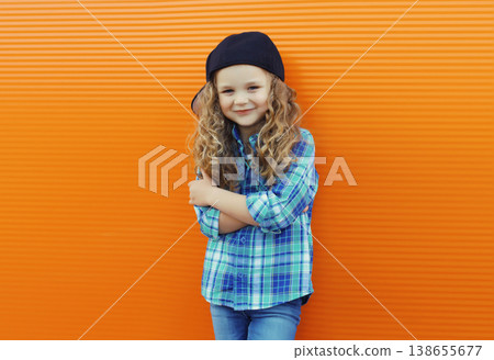 Happy cheerful kid girl dancer with curly hair, joyful child dancing in the city on orange wall Happy cheerful kid girl dancer with curly hair, joyful child dancing in the city on orange wall 138655677
