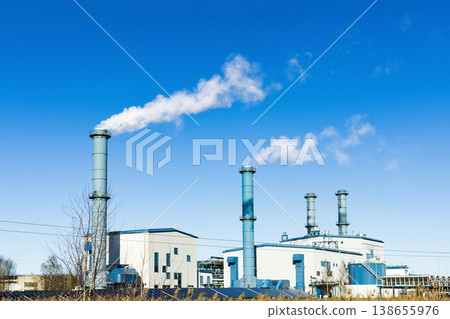 Thermal power plant emitting smoke from tall chimneys with solar panels in the foreground under a blue sky. Symbolizes electricity generation, ecology, and the energy crisis. Thermal power plant emitting smoke from tall chimneys with solar panels in the foreground under a blue sky. Symbolizes electricity generation, ecology, and the energy crisis. 138655976