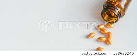 Amber bottle spilling golden softgel capsules on white background, representing medicine, vitamins, and skincare. Bottle spilling golden pills for health and beauty 138656240