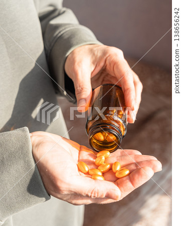 Person pouring orange health capsules from a brown bottle into an open palm, taking daily vitamins for wellness. Healthy lifestyle, self-care 138656242