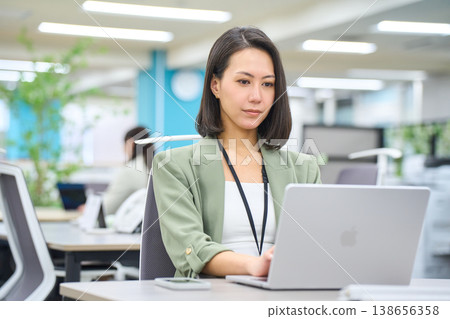 A smiling foreign businesswoman working on her laptop in a brightly lit office. 138656358