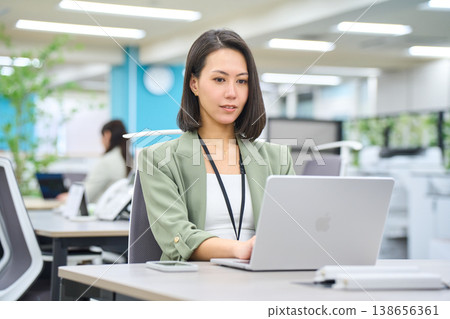 A smiling foreign businesswoman working on her laptop in a brightly lit office. 138656361