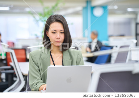 A smiling foreign businesswoman working on her laptop in a brightly lit office. A smiling foreign businesswoman working on her laptop in a brightly lit office. 138656363